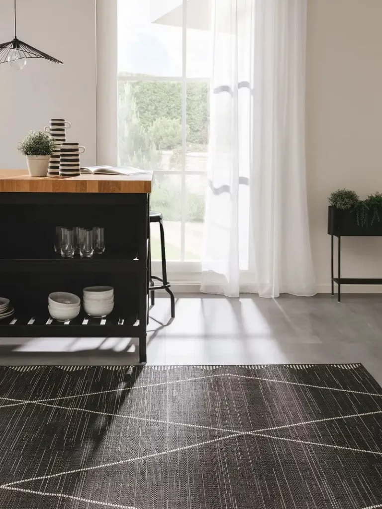 A cozy corner with a wooden countertop, black cabinetry, wall-mounted plants, and a striped beige and black rug on a grey floor.