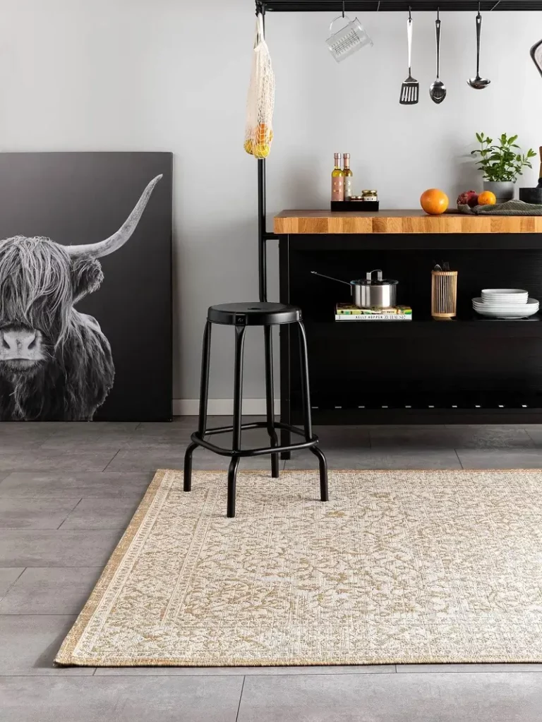 A well-lit dining area featuring sheer curtains, a wooden table with black legs, and a black and white geometric rug on a grey tiled floor.