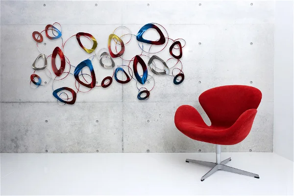 Modern interior with abstract metal wall art and red chair.