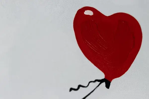 A close-up of a red heart-shaped balloon against a plain white background, part of an abstract painting.
