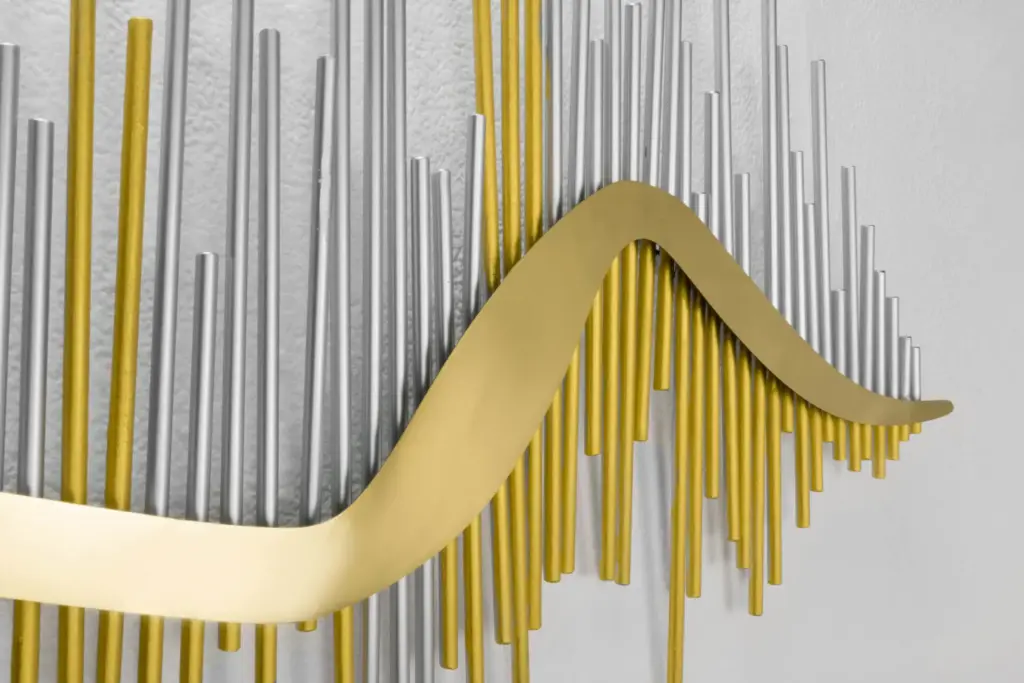 A close-up of a 3D wall sculpture featuring a flowing, golden ribbon-like shape over vertical white and gold textured lines.
