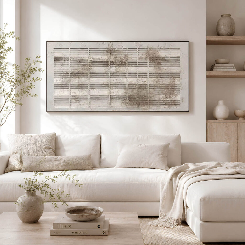 A large, horizontal textured abstract painting on a bright wall above a white sofa in a minimalist, Wabi-Sabi style living room.